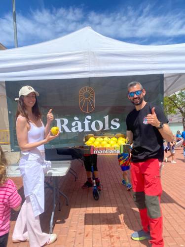 Dos personas posan frente a una carpa de Fruits Ràfols mostrando manzanas amarillas Mantiana durante un evento al aire libre.