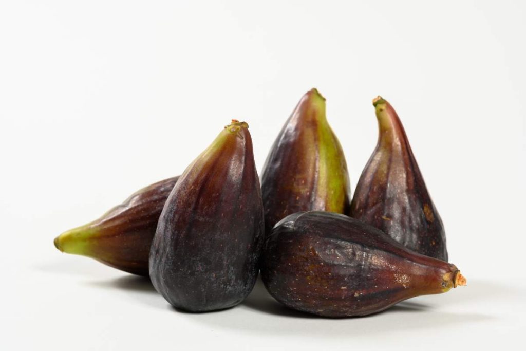 Cinco higos enteros de piel morada sobre fondo blanco.
