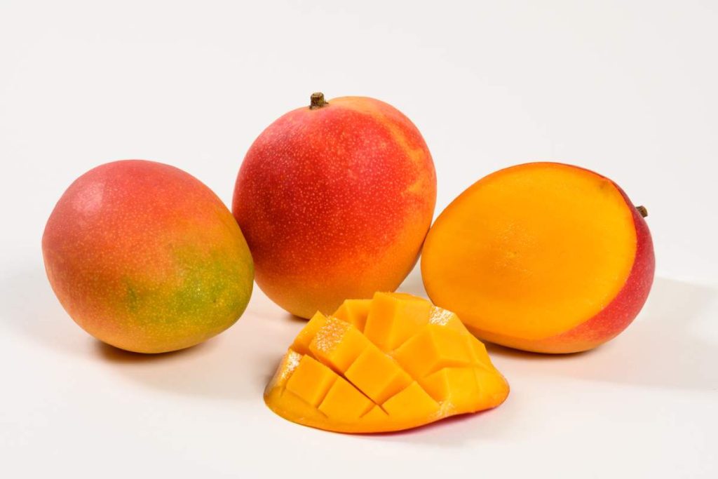 Dos mangos enteros, medio mango y una porción de pulpa cortada en dados.