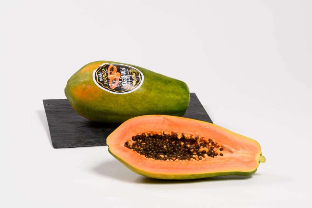 Papaya Reserva Gourmet entera y media papaya abierta, con pulpa naranja y semillas negras.