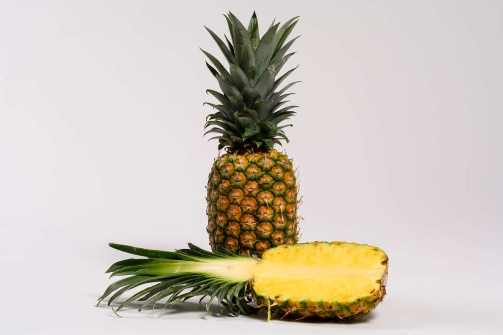 Piña entera junto a media piña cortada longitudinalmente.