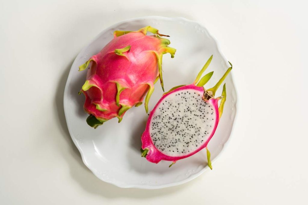 Pitahaya entera y media pitahaya cortada, con pulpa blanca y semillas negras, sobre un plato blanco.